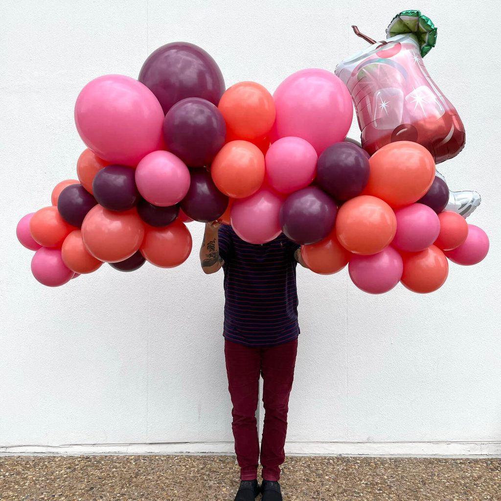 Rose, coral, and burgundy balloons make up this garland with a pink cocktail drink on top from Just Peachy in Arkansas.